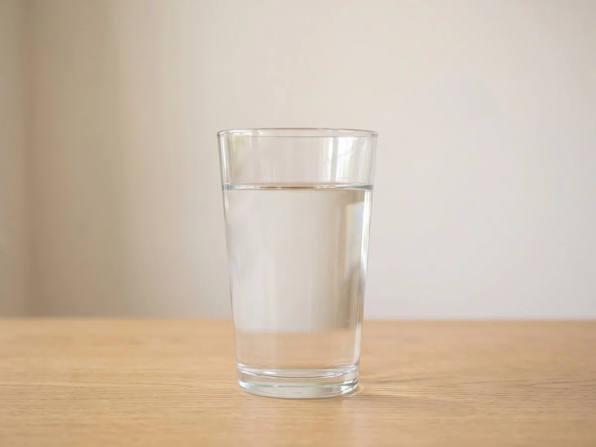 A clear glass tumbler of tap water standing at room temperature before choosing when to water the plant.